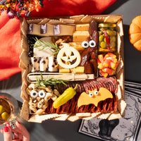 small halloween-themed charcuterie board featuring festive cheeses shaped like a pumpkin and bat, surrounded by assorted snacks and decorations