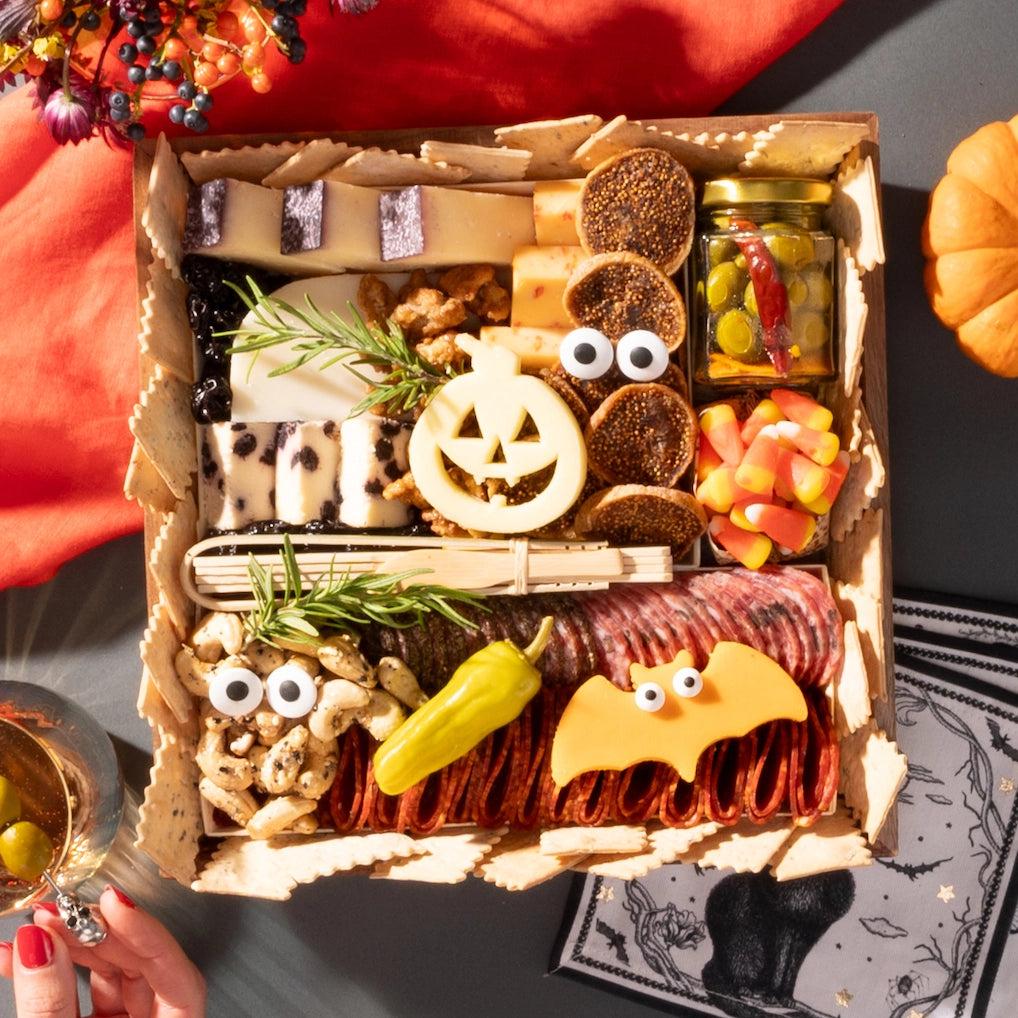 small halloween-themed charcuterie board featuring festive cheeses shaped like a pumpkin and bat, surrounded by assorted snacks and decorations