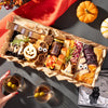 medium size halloween charcuterie board featuring festive cheese shapes, candy corn, meats, and nuts, with pumpkins and cocktails nearby
