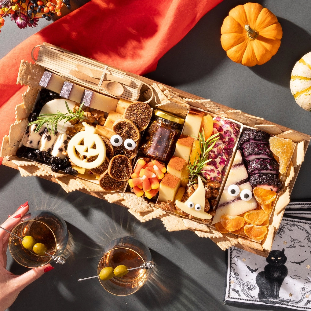 medium size halloween charcuterie board featuring festive cheese shapes, candy corn, meats, and nuts, with pumpkins and cocktails nearby