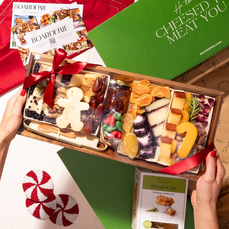 Holiday-themed medium cheese board with festive cheese shapes, nuts, dried fruits, and crackers, tied with a red ribbon and boxed with artisan crisps