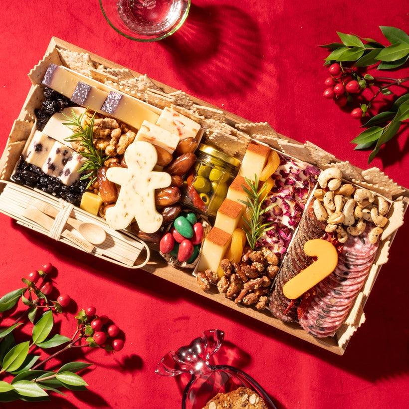 Festive Christmas charcuterie board with cheeses, nuts, dried fruits, and gingerbread man and candy cane-shaped cheese on a red background.