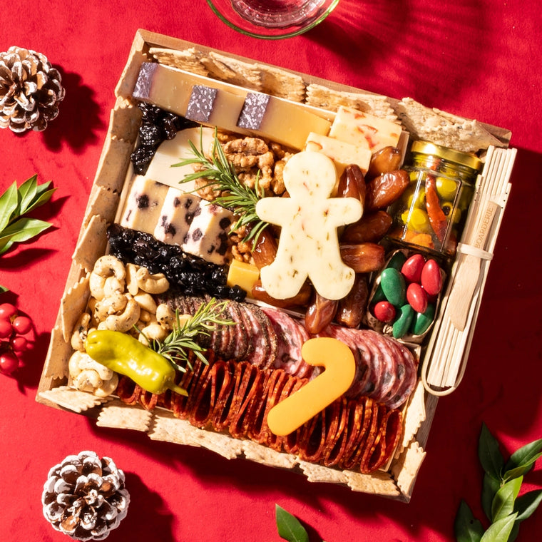 small holiday-themed charcuterie board gift featuring cheeses shaped like a gingerbread man &amp; candy cane, nuts, meats, and festive garnishes