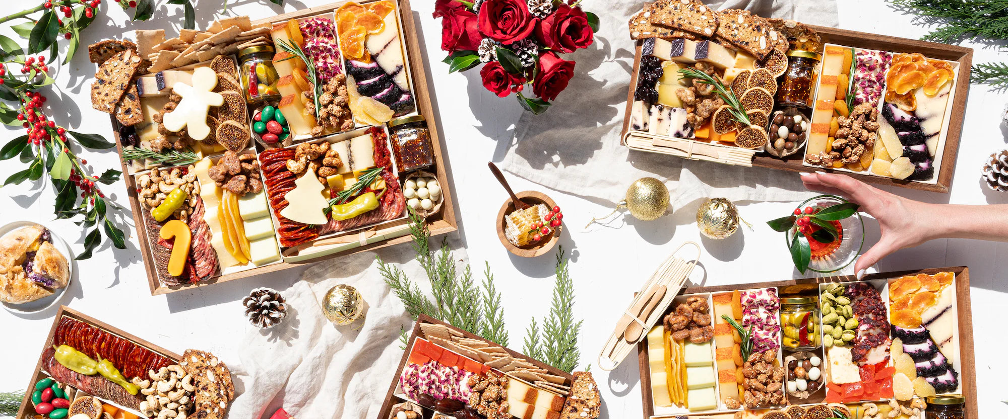 Festive charcuterie boards with assorted cheeses, meats, nuts, and holiday decorations on a white background.