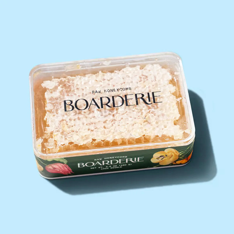 Raw honeycomb in clear plastic Boarderie container against light blue background.