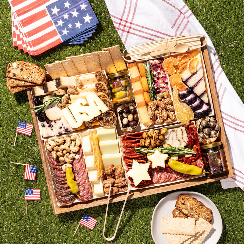 labor day themed charcuterie board with assorted cheeses, meats, nuts, & crackers, featuring cheese cutouts shaped like "USA" & stars