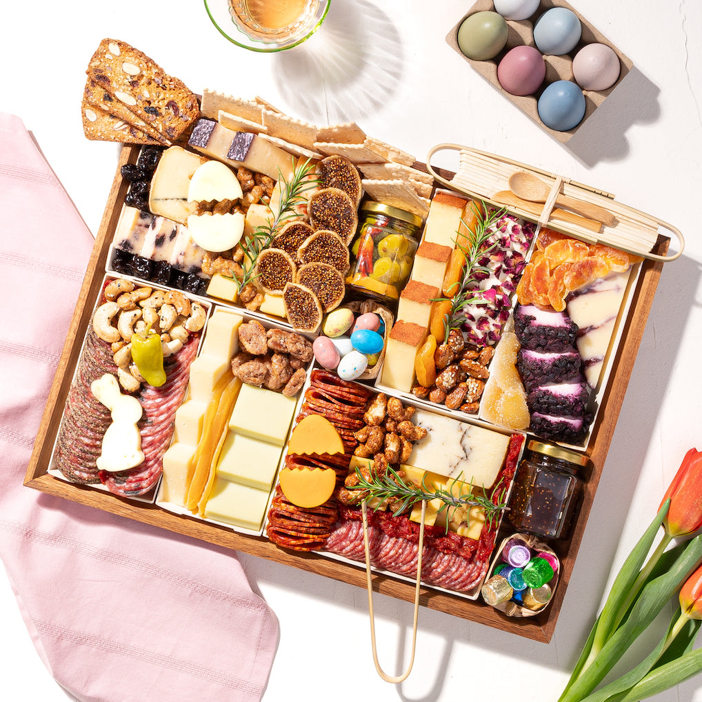 Festive charcuterie board with assorted meats, cheeses, crackers, and decorative pastel candies, set on a spring-themed table.