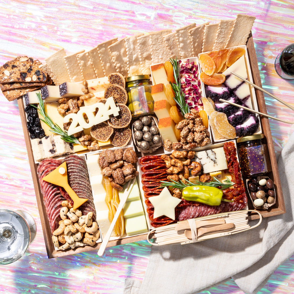 Large New Year's charcuterie board featuring assorted cheeses, meats, nuts, dried fruits, & decorative cheese cutouts shaped as "2024"