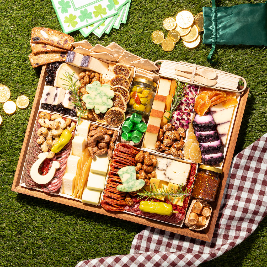 St. Patrick's Day charcuterie board featuring cheeses, meats, nuts, and shamrock & horseshoe-shaped cheese pieces, set on grass with themed decorations