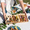 Person placing a charcuterie board with meats, cheeses, and crackers on an elegantly decorated outdoor table.