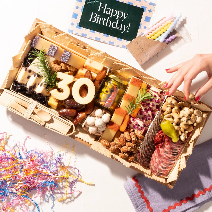 Birthday charcuterie board featuring "30" cheese numbers, a variety of cheeses, meats, nuts, and festive decorations like colorful candles and confetti.