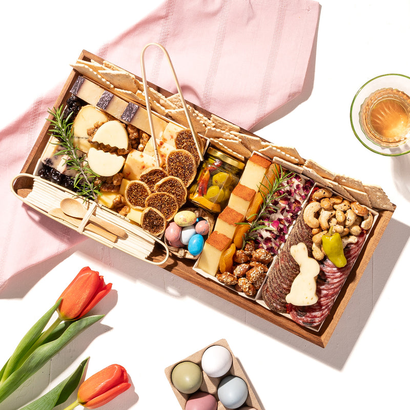 Spring-themed charcuterie board with cheeses, meats, nuts, and pastel candies, decorated with a cheese bunny shape and tulips.