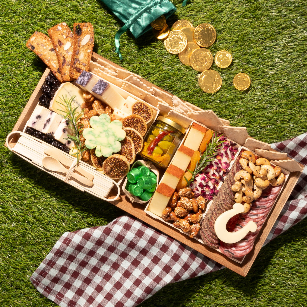 medium St. Patrick's Day-themed charcuterie board featuring cheeses, meats, nuts, a shamrock-shaped cheese piece, & a horseshoe-shaped cheese, set on grass