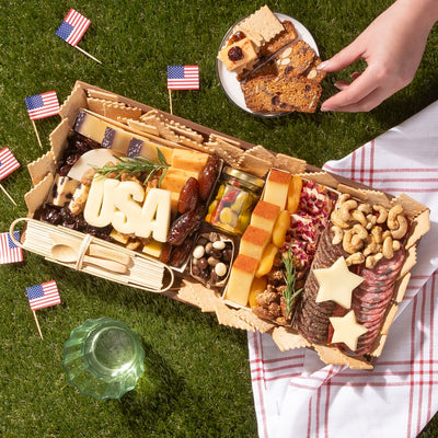 Memorial Day charcuterie board with meats, cheeses, nuts, and patriotic cheese cutouts spelling “USA” and shaped like stars.