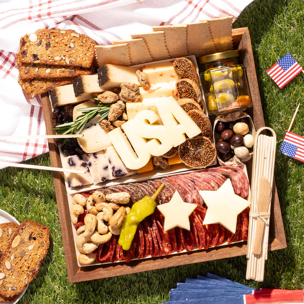 memorial day charcuterie board with assorted cheeses, meats, nuts, & crackers, featuring cheese cutouts shaped like "USA" & stars