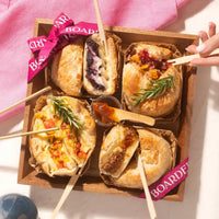 Mother’s Day charcuterie featuring baked brie pastries filled with assorted toppings and fig marmalade in a wooden box.