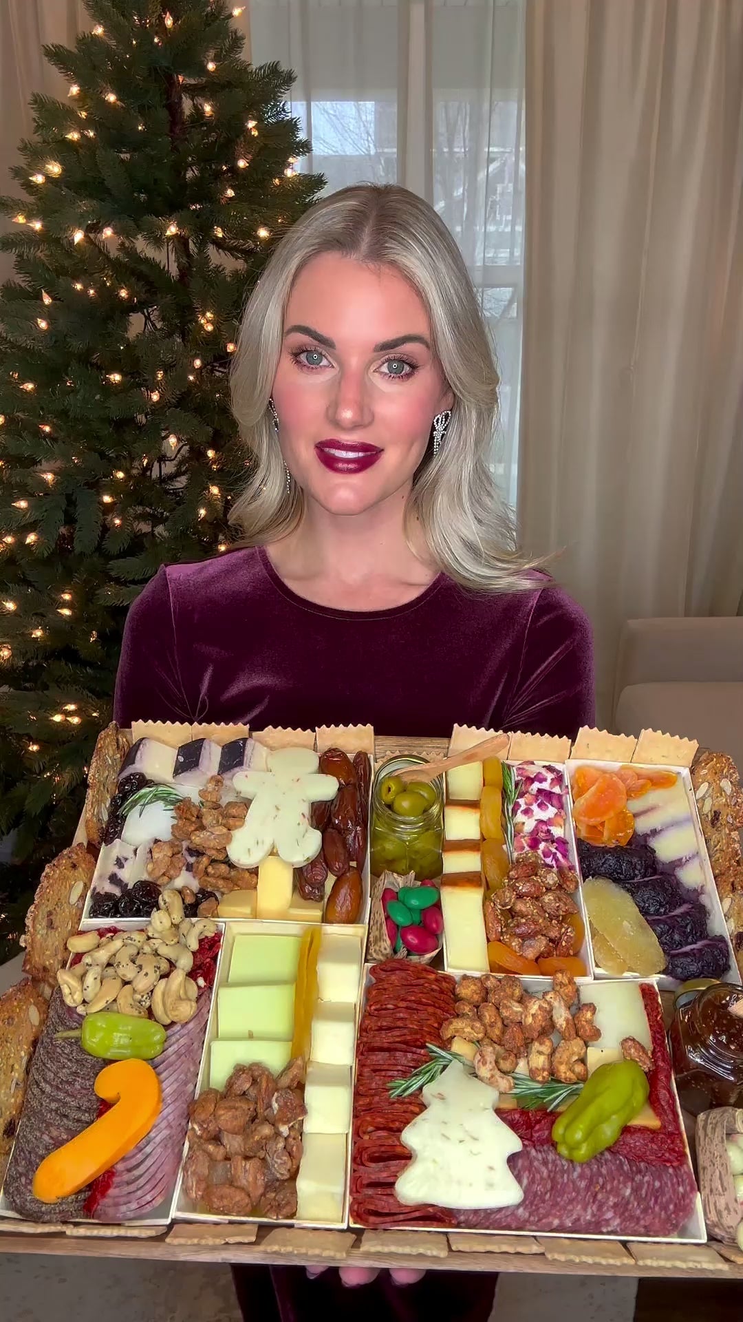 Woman presenting Boarderie's premade charcuterie board inside home with holiday decorations.