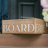 Charcuterie board delivery box from Boarderie placed on a doorstep, featuring gourmet cheese and meat selections.