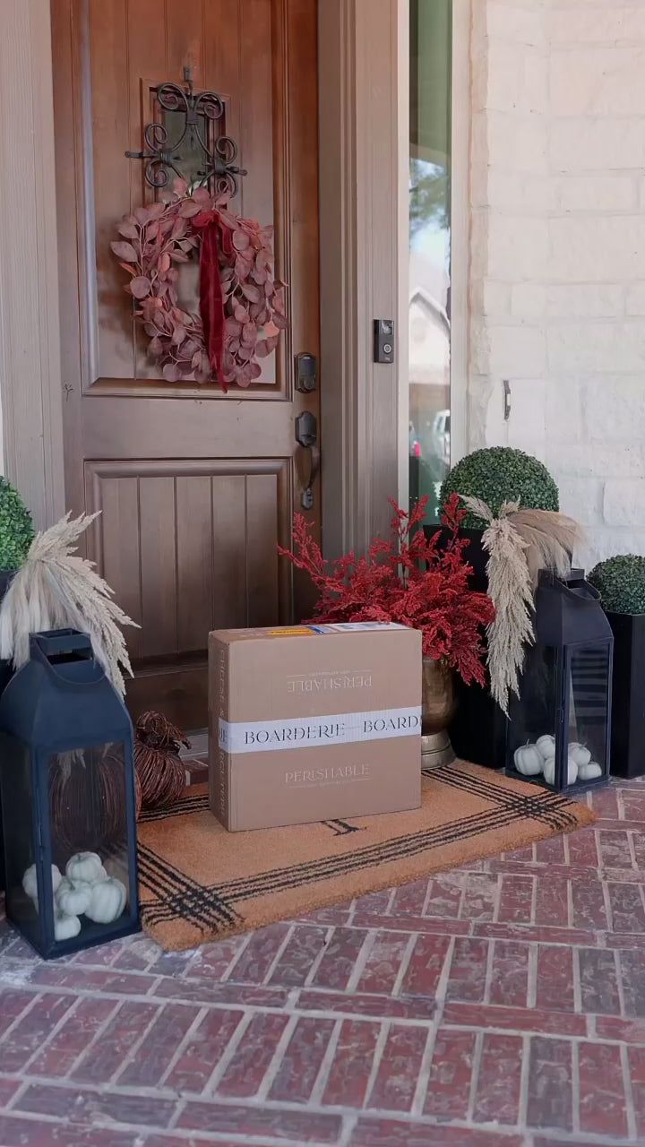 Box delivered to door with Thanksgiving decorations around the box. Girl unboxing Thanksgiving cheese & charcuterie board and putting it on table.