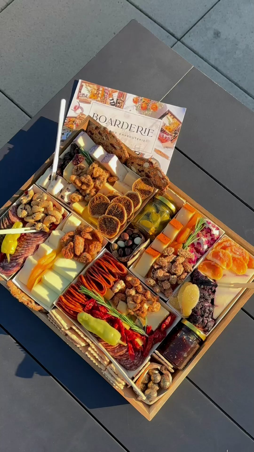 Woman unboxing a Boarderie charcuterie board on a black table with festive music playing.