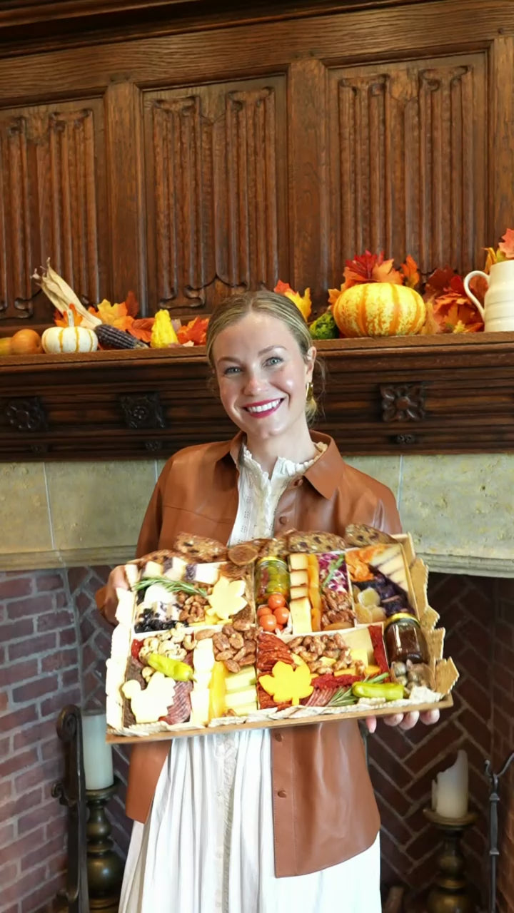 Cheese and charcuterie board thanksgiving edition being held by blonde girl with fall decorations around her. Unboxing of board and placing the charcuterie board on a table for Thanksgiving.