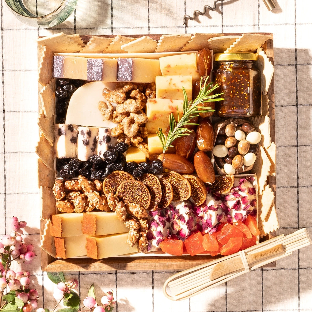 small cheese board gift with a selection of cheeses, crackers, nuts, dried fruits, figs, dates, & a fig jam jar