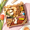 Easter-themed charcuterie board with cheese, meats, nuts, pastel eggs, and decorative egg and bunny cheese shapes, accented with tulips.