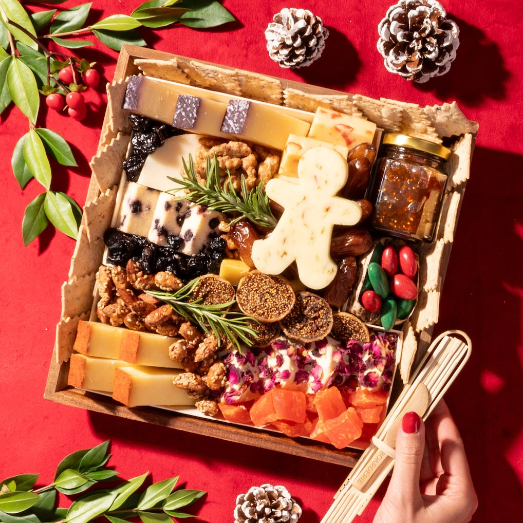 small holiday cheese board with festive cheese shapes, nuts, dried fruits, fig jam, and crackers on a red tablecloth