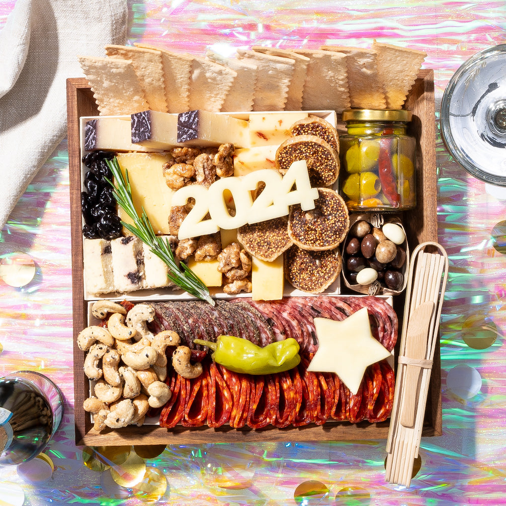 New Year-themed small charcuterie board with cheese, meats, nuts, figs, crackers, & "2024" carved from cheese on a festive background