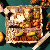 Thanksgiving charcuterie board for 2+ people with assorted cheeses, meats, crackers, dried fruits, & fall-themed decorations on a green tablecloth