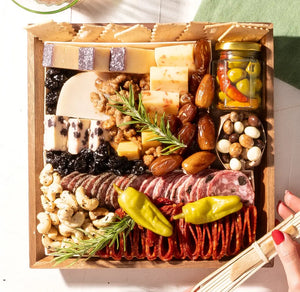 Premade charcuterie board with assorted cheeses, cured meats, olives, nuts, dried fruit, and rosemary on an acacia tray.