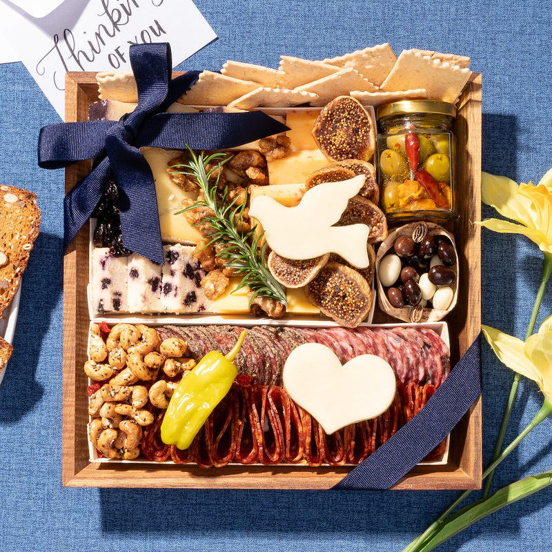 Sympathy charcuterie board with a dove-shaped cheese, nuts, & meats, arranged with a blue ribbon