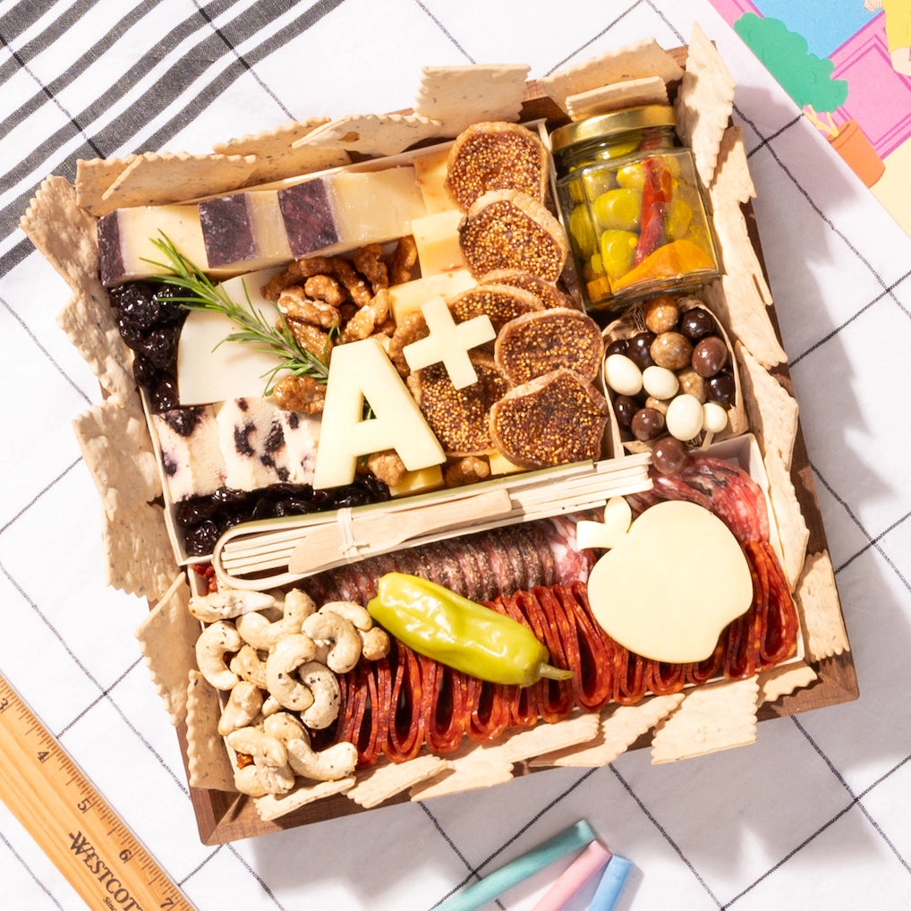 Small teacher-appreciation charcuterie board with cheese, meats, nuts, an "A+" cutout, & apple-shaped cheese on a checkered cloth