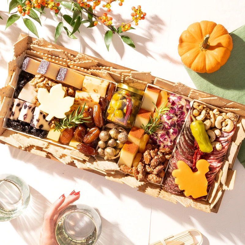 Thanksgiving-themed charcuterie board with cheeses, meats, nuts, dried fruits, & turkey-shaped cheese, surrounded by seasonal decor