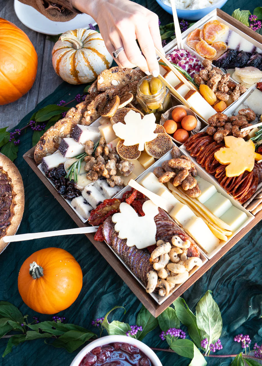 autumn-themed charcuterie board with cheeses, meats, nuts, and pumpkins, decorated with leaf-shaped cheese slices