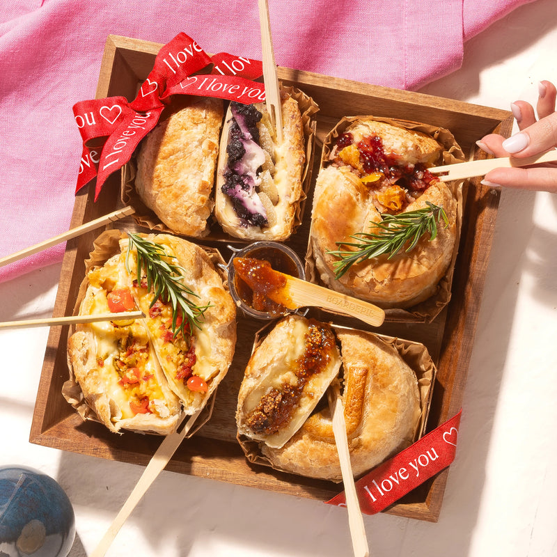 Valentine's baked brie board with decorated pastries, a red bow, fig jam, and romantic red roses.