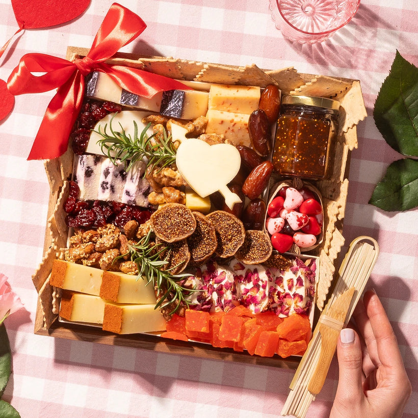 Valentine's Day small cheese board with heart-shaped cheese, dried fruits, nuts, and crackers on a pink checkered tablecloth.