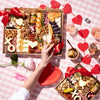 Valentine's Day charcuterie board with assorted cheeses, meats, nuts, & heart-shaped decorations on a pink checkered table