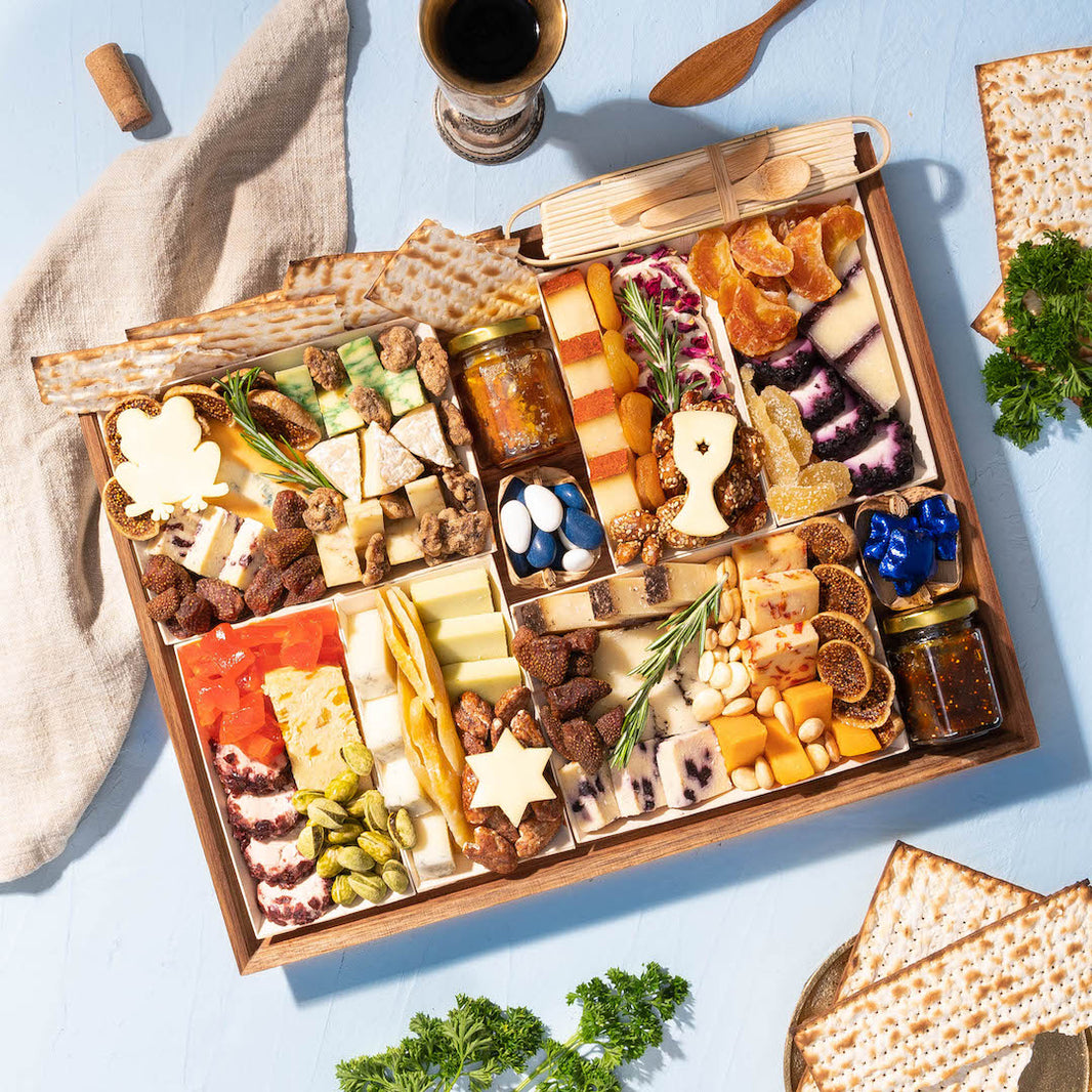 festive large charcuterie board loaded with various cheeses, dried fruits, nuts, crackers, & decorative jam jars