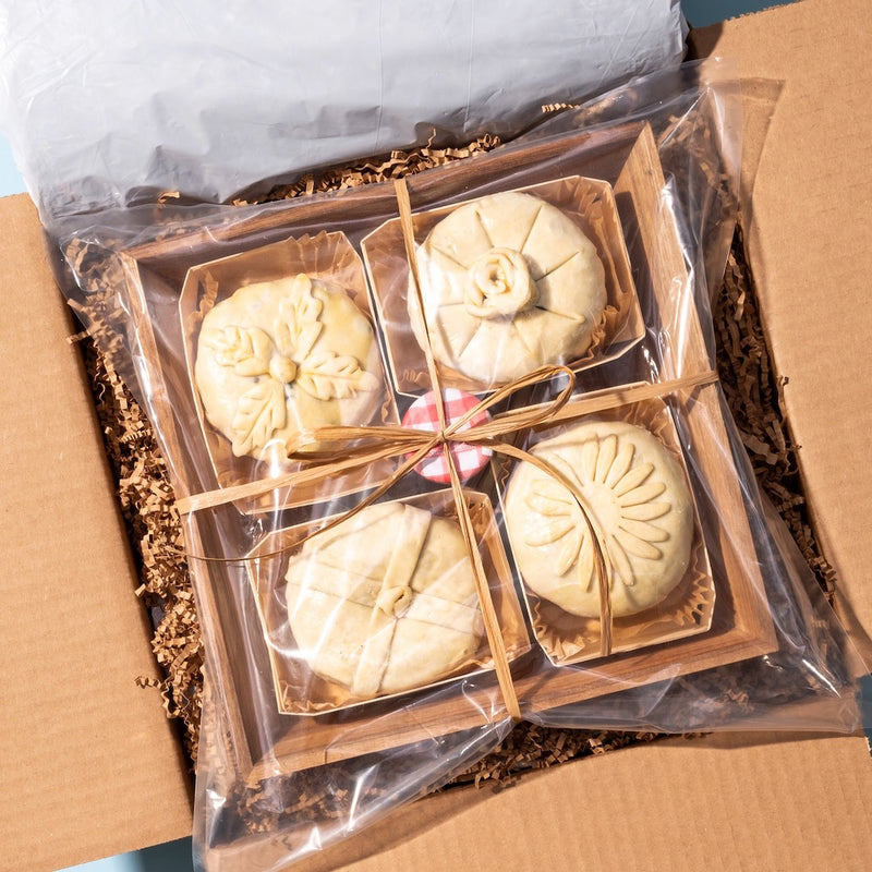 Unboxing a baked brie board with intricately decorated, uncooked pastries wrapped in plastic and tied with a ribbon.