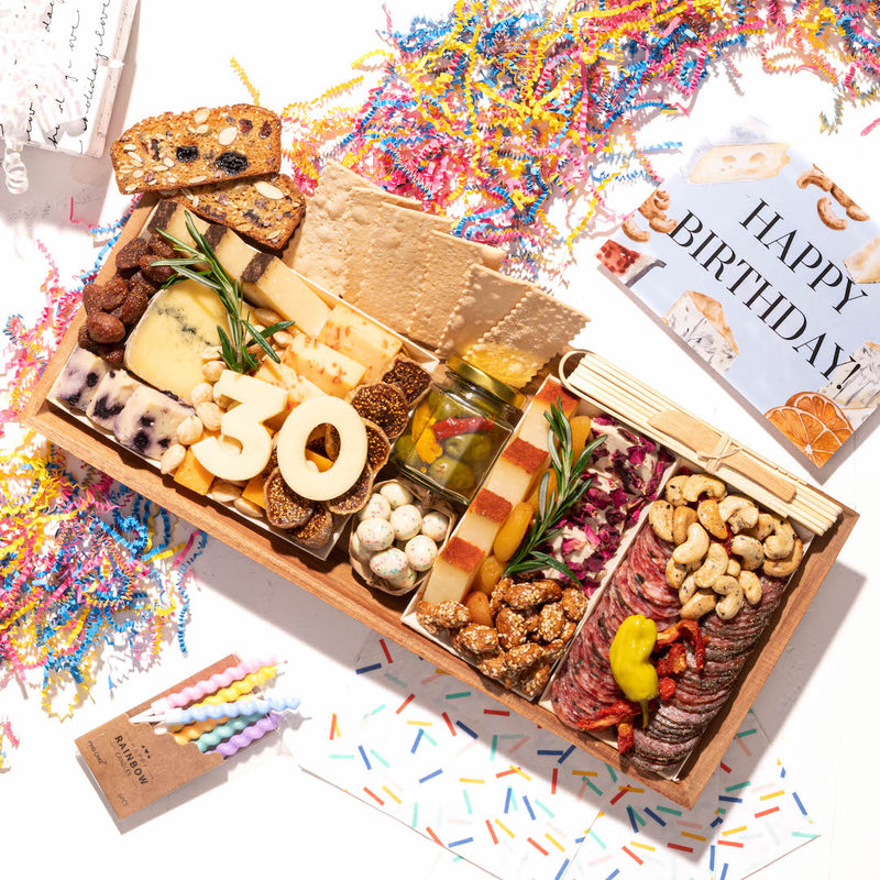 Festive charcuterie board with meats, cheeses, and "30" in cheese, surrounded by colorful confetti and birthday decorations.